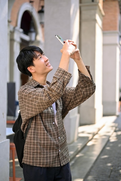 Asian man tourist enjoys strolling around the city square taking a picture with his phone