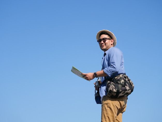 Asian man travel with map and vintage camera on blue sky background