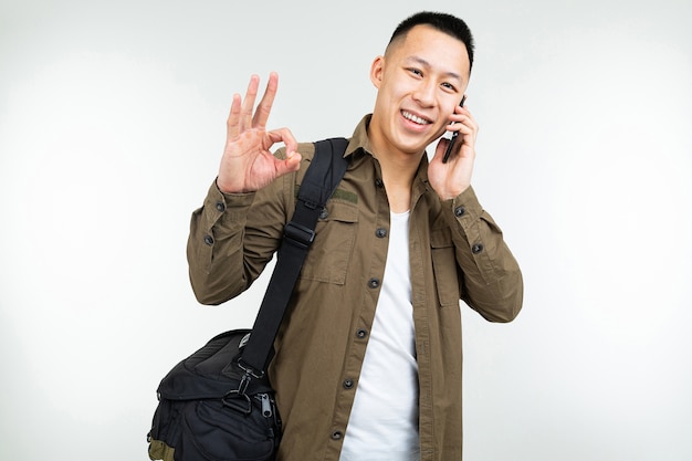 Asian man in urban clothes with a bag discusses business on the phone