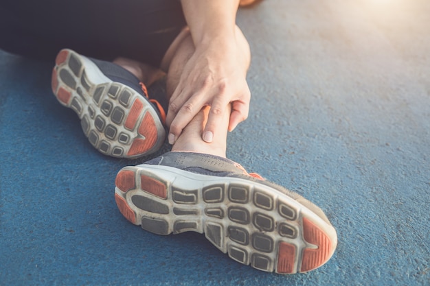 Asian man use hands hold on his ankle while running on road in the park. Focus on ankle.