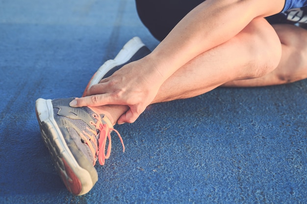 Photo asian man use hands hold on his ankle while running on road in the park