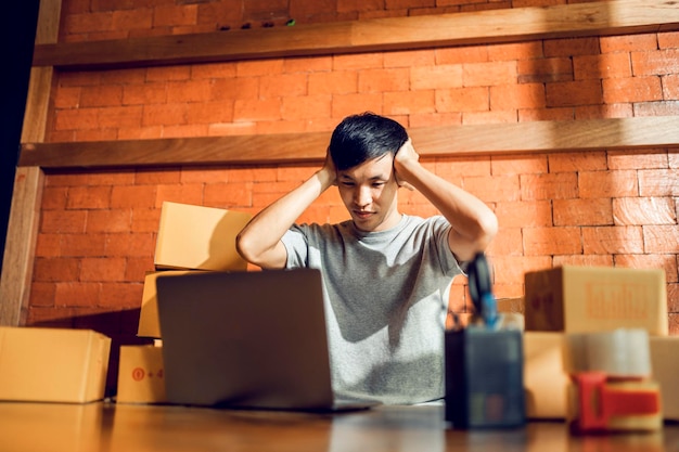 An Asian man uses a mobile phone to take orders and display items in a box that records live streaming video online at the store small business owner Asian online market delivery concept