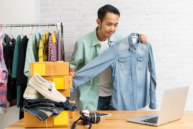 Asian man using computer laptop selling online denim shirt