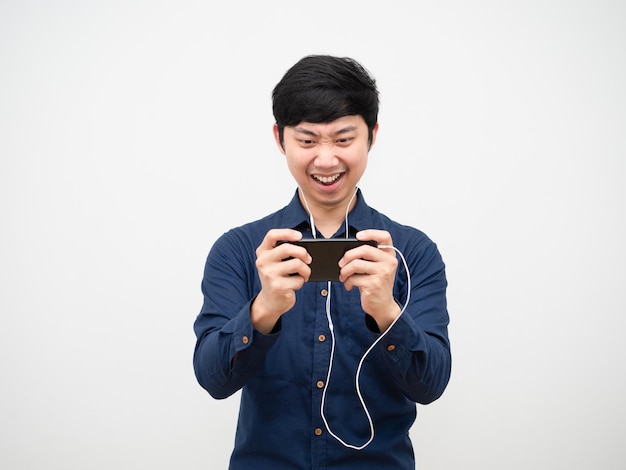 Азиатский мужчина, использующий наушники, играет в игру на мобильном телефоне, чувствуя себя весело на белом фоне