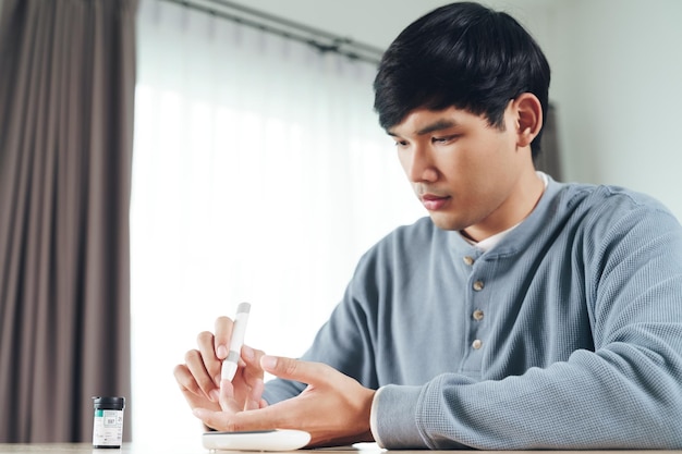 Asian man using lancet on finger for checking blood sugar level by Glucose meter