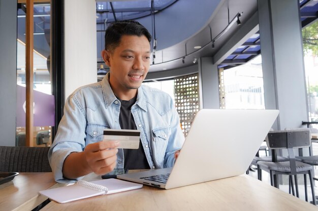 Foto uomo asiatico che usa un portatile e un telefono cellulare per fare acquisti online con carta di credito in un caffè online