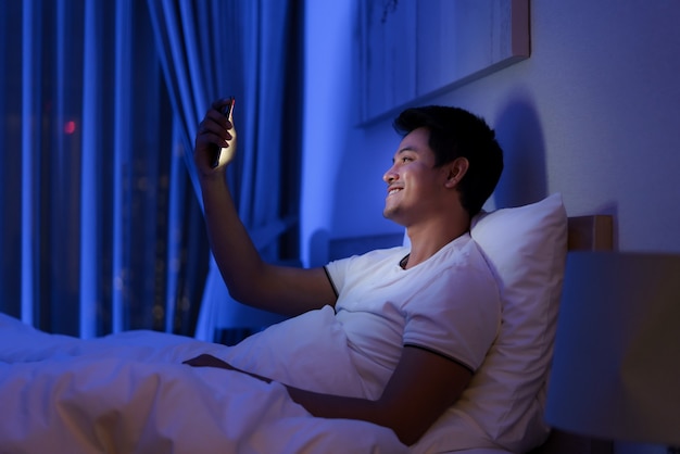 Asian man virtual happy hour meeting online together with his\
girlfriend in video conference to good night before sleep at night\
with smartphone for a online meeting in video call