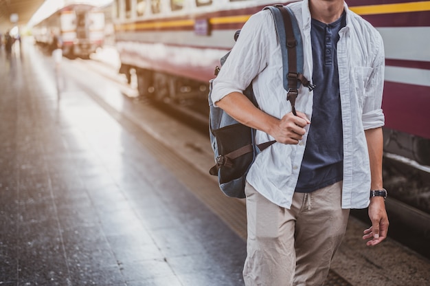 休暇のために駅で電車に歩いているアジア人男性。旅行の概念。駅を歩く男の旅行者観光客。