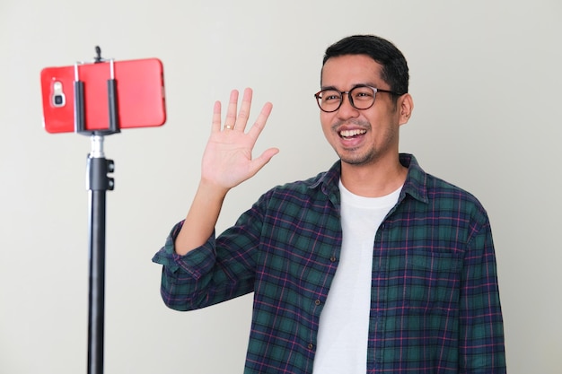 Asian man waving hand with happy expression when making content using his phone