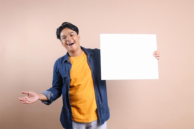 Фото Азиатский мужчина носит повседневную одежду и держит белую пустую доску для макета или рекламы с счастливым выражением лица