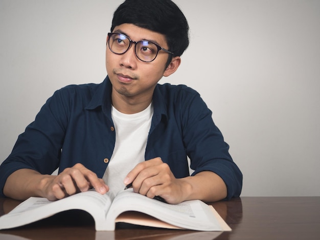 아시아 남자는 안경을 쓰고 탁자 위에 있는 책을 읽고 부드러운 미소를 짓는다