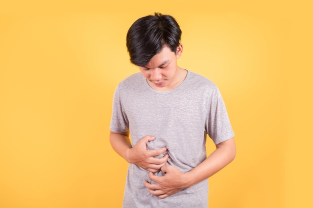 Asian man wear a Tshirt suffering from stomach ache because he has diarrhea on yellow background