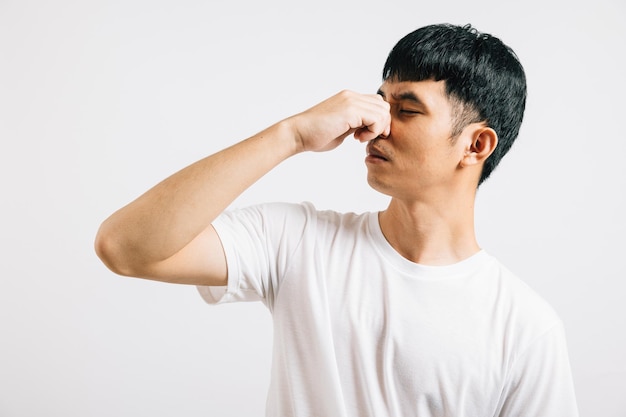 Asian man wearing an anxious expression while pinching his nose due to a strong and stinky odor