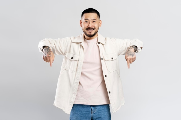 Asian man wearing casual clothes isolated on gray background pointing fingers down on copy space