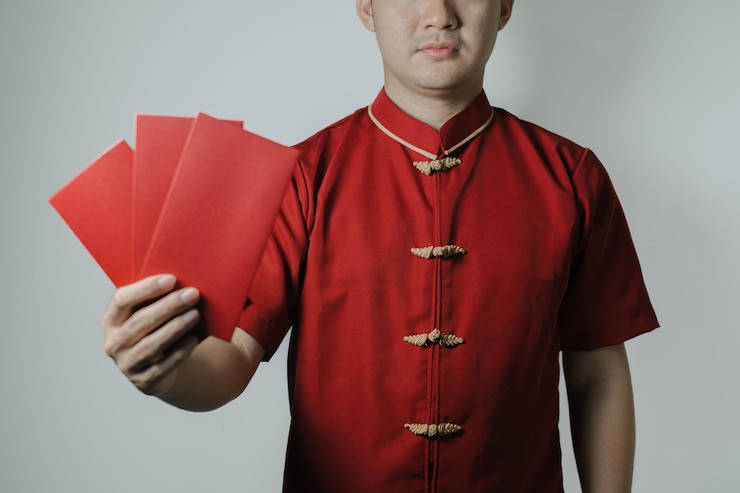 Photo asian man wearing cheongsam or chinese traditional cloth is holding angpao or red monetary gift and showing it to the camera on white background gong xi fa cai