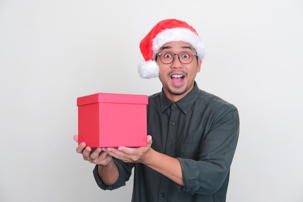 Asian man wearing Christmas hat holding a box of gift with amazed expression