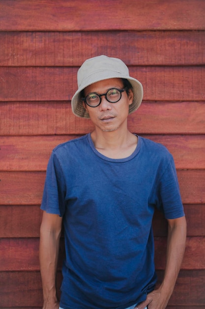 Asian man wearing clothes hat standing against brown wood wall