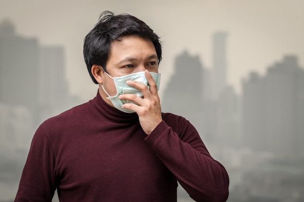 높은 아파트의 발코니에서 대기 오염에 대한 얼굴 마스크를 쓰고 아시아 남자