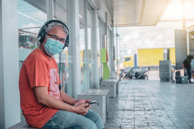 アジア人男性の携帯電話のライフスタイルを保持している身に着けているフェイスマスク新しい通常の社会的距離