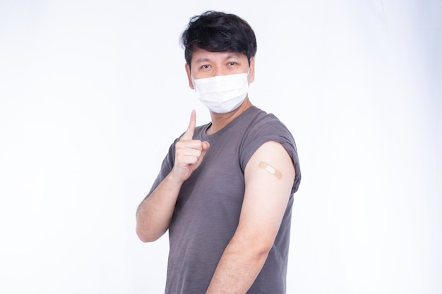 Asian man wearing face mask showing  shoulder with bandage and show thumps up for the first getting vaccination covid-19 immunization, isolated on white background