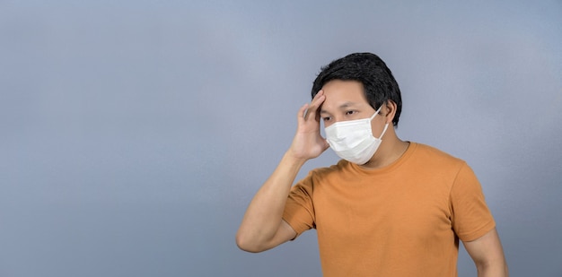 asian man wearing face surgical mask headache and worry on blue background coronavirus pandemic