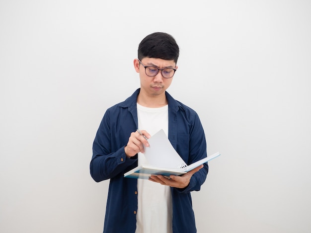 Uomo asiatico con gli occhiali che legge il libro in mano faccia seria su sfondo bianco isolato