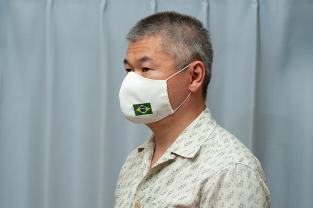 Asian man wearing homemade cloth mask with brazil flag for\
protection against coronavirus