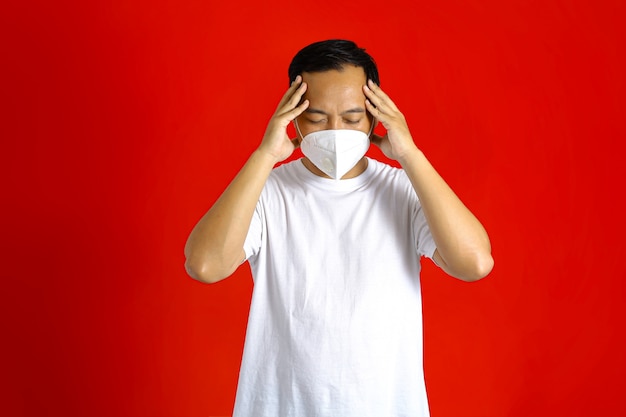 Asian man wearing a medical mask having a headache while holding his head with both hands