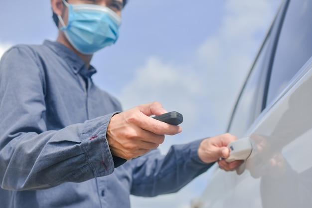 Asian man wearing medical mask and holding key to opening car\
door