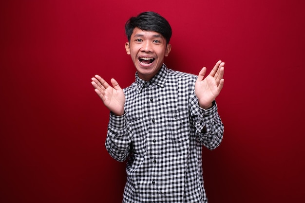 Asian man wearing plaid shirt with shocked expression on red background