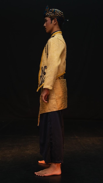 An Asian man wearing a traditional costume with beautiful motifs on his shirt and wearing a bandana called a bendo in a room