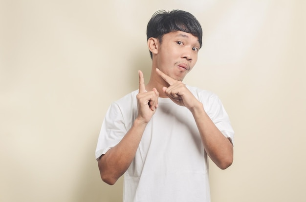 Asian man wearing white tshirt with gesture pointing at empty space on isolated background