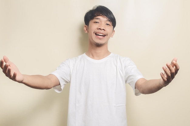 Asian man wearing white tshirt with welcome gesture isolated background