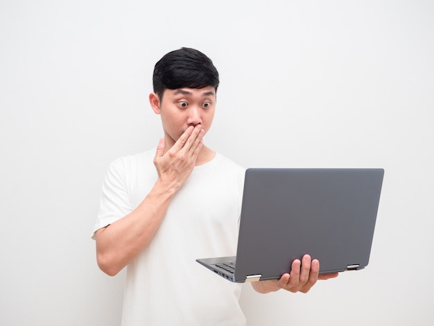 Азиатский мужчина в белой рубашке закрывает рот с шокированным лицом, глядя на ноутбук в руке на белом изолированном