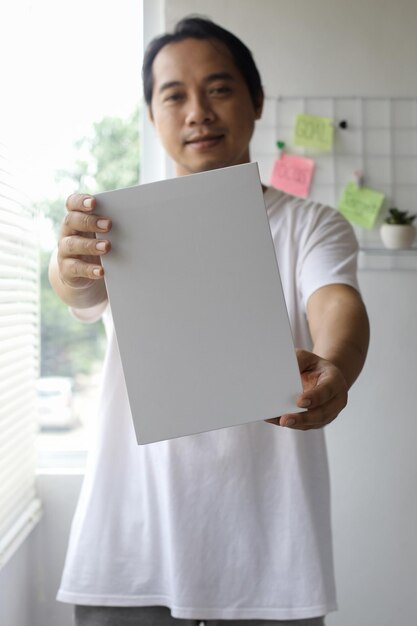 asian man in white tshirt is holding white paper for mock up