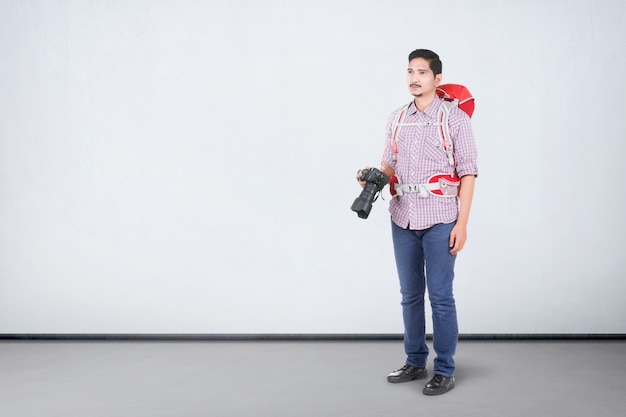 Asian man with a backpack holding a camera to take pictures
