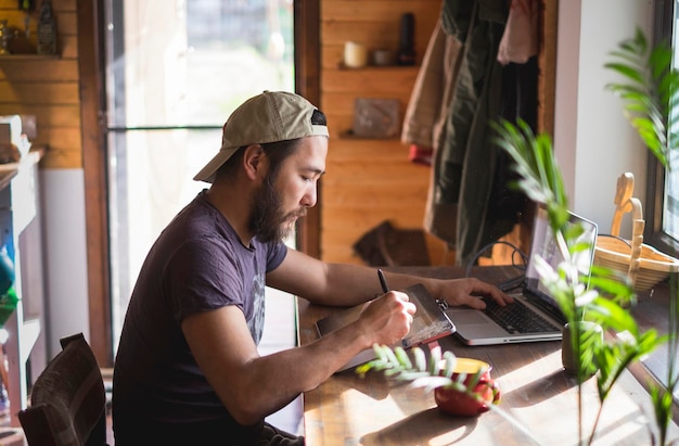 Photo asian man with beard working on a tablet and a laptop at home