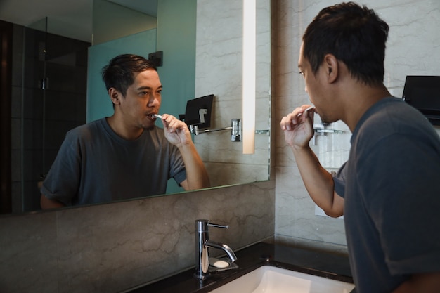 Asian man with brushing teeth and looking mirror in the bathroom