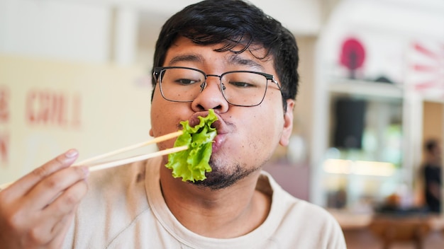 안경을 쓴 아시아 남자는 레스토랑에서 맛있는 상추를 먹는다