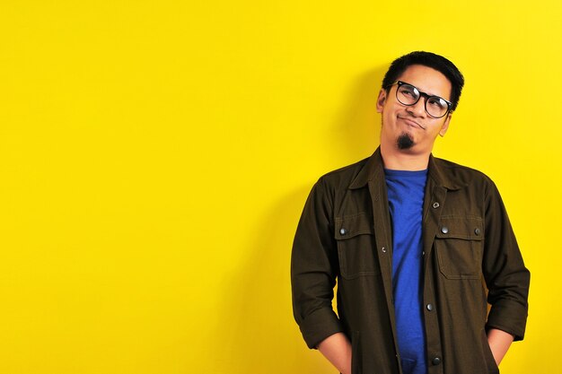 Азиатский мужчина с юмористическим лицом или забавным лицом смотрит на копировальное пространство, изолированное на желтом фоне