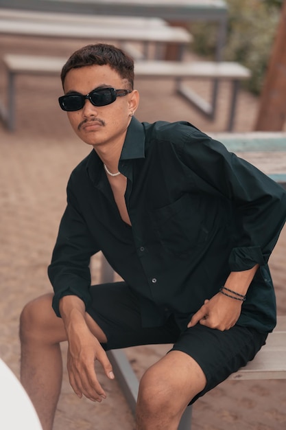An Asian man with a mustache face wearing a shirt and sunglasses while hanging out with his friends in a cafe