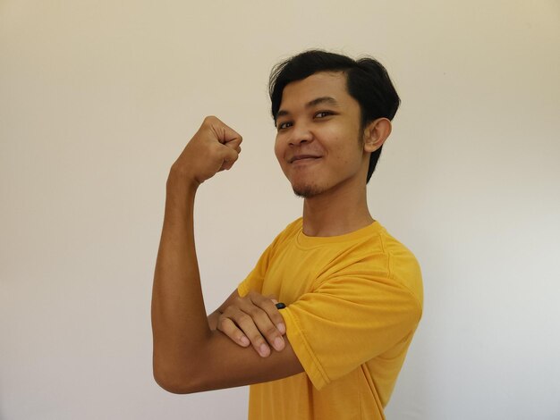 強いジェスチャーを持つアジア人男性が腕の筋肉を握る