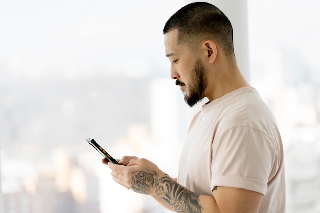 Asian man with stylish tattoos holding smartphone using mobile app shopping online at home