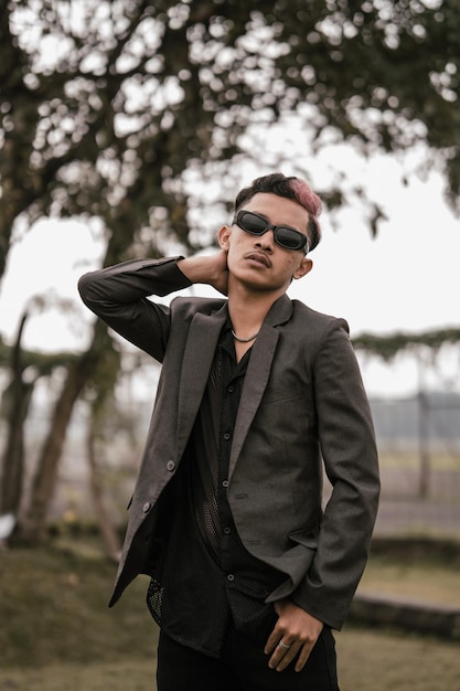 An Asian man with sunglasses posing in a gray suit in the yard