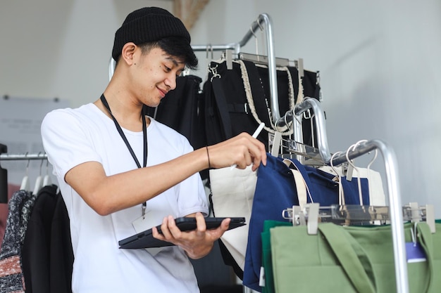 Asian man working as shop assistance at retail shop holding digital tablet for checking stocks