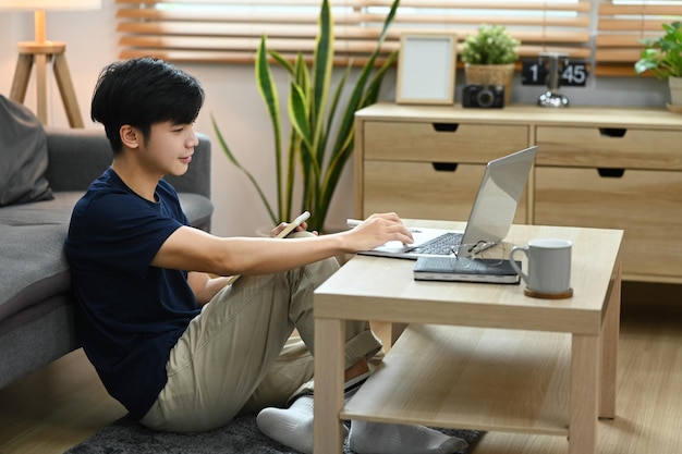 Asian man working online from home with laptop computer sitting in bright living room