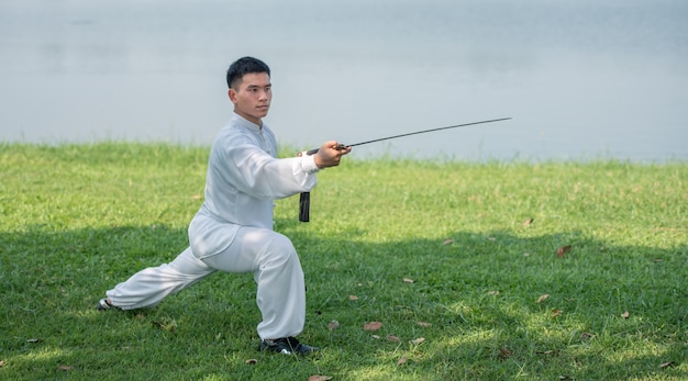 朝の公園、中国の武道、生活概念の健康管理で太極拳の剣でワークアウトアジア人