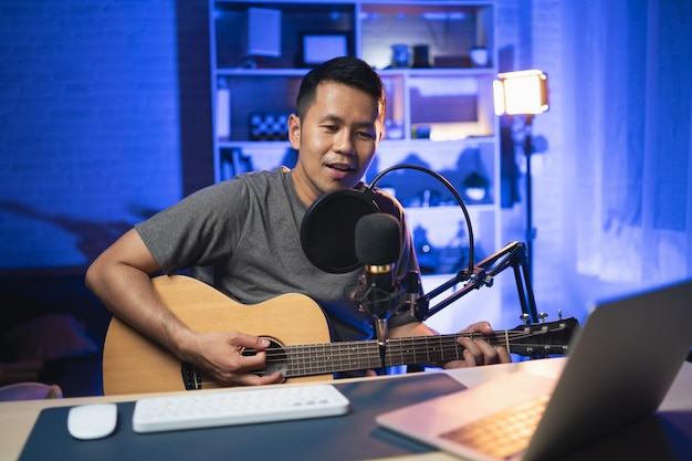 Asian man youtuber live streaming perfomance playing guitar and sing a song Asian man teaching guitar and singing online Musician recording music with laptop and playing acoustic guitar