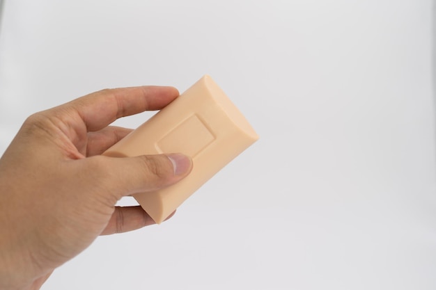 Asian mand hand holds rectangle cream color soap in studio light on white clear background