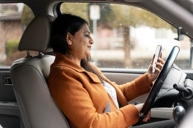 Il tassista femminile maturo asiatico che utilizza lo smartphone controlla l'app mobile mentre si trova nel parcheggio